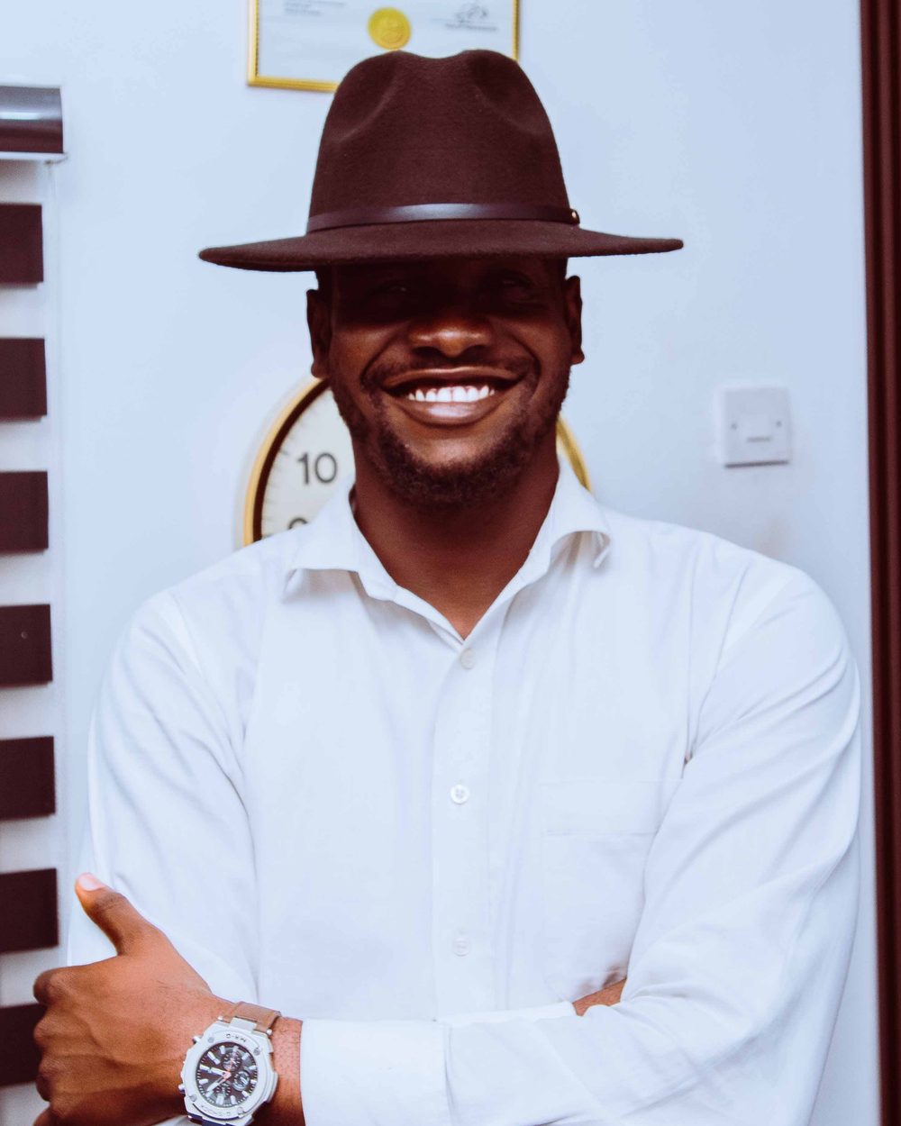 Ibinabo Martins, smiling in a brown fedora and white shirt
